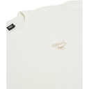 An off-white ribbed cotton t-shirt featuring a small beige embroidered Stussy logo on the left chest, with a black brand tag visible inside the collar.