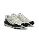 A pair of Asics athletic sneakers in off-white and black, featuring the brand's signature stripe logo on the side, set against a plain white background.