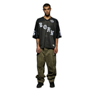 A male model stands against a plain white background wearing a black oversized jersey-style t-shirt with 'BORN' printed in white across the chest, olive green cargo pants, and black shoes.