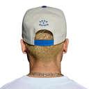 Back view of a person wearing a light gray baseball cap with blue 'ROCK N' RISEN' embroidery on the back and a blue adjustable strap, shown against a plain white background.
