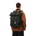 A man viewed from behind wearing a dark olive green Carhartt backpack over a brown jacket, set against a plain white background.