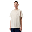 A man wearing a light beige Carhartt short-sleeve t-shirt with a small embroidered logo on the left chest, paired with dark blue jeans, against a plain white background.