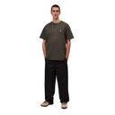 A man modeling a dark olive green short-sleeve t-shirt with a small gold Carhartt logo on the left chest, paired with black pants and beige sneakers, against a plain white background.