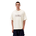 A man wearing an off-white Carhartt short-sleeve t-shirt with a gray logo on the chest, paired with dark blue jeans, against a plain white background.
