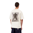 A man viewed from behind wearing an off-white Carhartt t-shirt with a large black graphic print on the back, paired with dark blue jeans, against a plain white background.