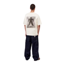 A model viewed from the back wearing a cream-colored Carhartt t-shirt with a large black graphic print and the brand name 'CARHARTT' on the back, paired with dark blue jeans.