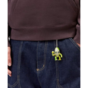 A close-up of a person wearing a dark brown sweatshirt and dark blue jeans, with a small green alien-shaped keychain hanging from the pocket.