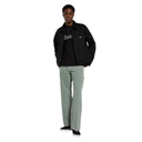 A model wearing a black jacket over a black graphic t-shirt, paired with sage green wide-leg jeans and black sneakers, standing against a solid white background.