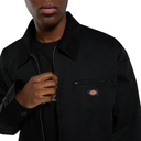 A close-up of a person wearing a black Dickies work jacket over a black t-shirt, with the brand logo visible on the chest pocket.