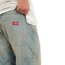 Close-up of a person wearing light blue denim work pants with a red Dickies logo patch on the back pocket, paired with a white t-shirt, against a white background.
