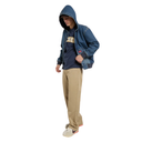 A model wearing a blue denim zip-up hoodie over a navy blue Nike t-shirt, paired with beige pants and white sneakers, shown against a plain white background.