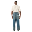 A man viewed from behind wearing light-wash blue wide-leg jeans with a circular embroidered logo on the back pocket and a cream-colored t-shirt, against a plain white background.