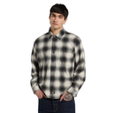 A man wearing a long-sleeve plaid button-up shirt in black and off-white, paired with dark blue jeans, against a solid white background.