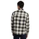 A man viewed from behind wearing a long-sleeve black and off-white plaid flannel shirt and dark blue jeans, set against a plain white background.