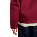 Close-up of a person wearing a burgundy jacket over a cream ribbed shirt and dark blue jeans, shown from the back against a white background.