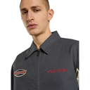 Person wearing a dark gray work shirt with embroidered logos on a white background