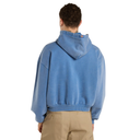 A man viewed from behind wearing a cropped, washed blue hoodie and khaki pants against a plain white background.