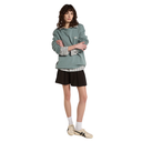 Person wearing a green sweater, plaid shirt, and black shorts on a white background