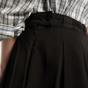 Close-up of black pleated pants with a plaid shirt in the background
