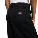 Close-up back view of a person wearing black Dickies work pants, showing the back pocket and the brand patch on the upper left side.