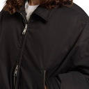 Close-up of a person wearing a black zip-front jacket over a white shirt, with brown hair visible at the collar.