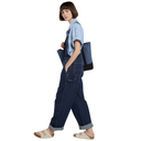 Person wearing blue denim overalls and a light blue shirt, holding a blue bag on a white background