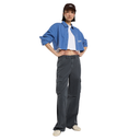 A model stands against a solid white background wearing a blue cropped button-up shirt over a white t-shirt, dark gray cargo pants, a brown baseball cap, and off-white sneakers.