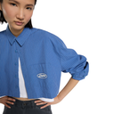 A model wearing a blue and white pinstriped cropped button-up shirt with a chest pocket and a white embroidered 'Aloha' logo, styled over a white undershirt and dark jeans against a white background.