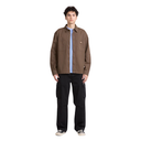 A model stands against a solid white background wearing a brown utility-style overshirt over a light blue button-up shirt, paired with black cargo pants and gray sneakers.