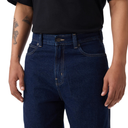 A close-up of a person wearing dark indigo blue denim jeans and a black t-shirt, showing the front waistband, belt loops, and front pockets against a white background.