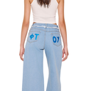 Light blue jeans with blue lettering on the back pocket worn by a person.