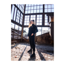 Person in black outfit standing in an industrial setting with large windows.