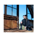 Person in black outfit crouching in an industrial setting with large windows and blue sky.