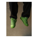 Green sneakers worn with black pants on a plain background