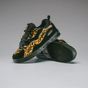 A pair of black low-top sneakers with a bold yellow and black leopard print pattern on the overlays, displayed on a neutral gray studio background.