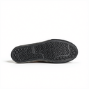 The black rubber outsole of a slip-on shoe, showing a textured herringbone pattern and a debossed brand logo, photographed on a clean white background.
