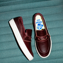 Pair of maroon slip-on shoes with white soles on a textured teal surface