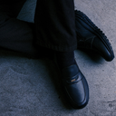 Black loafers worn with black pants on a concrete floor