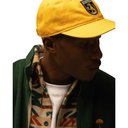 Person wearing a yellow cap with a logo, green jacket, and patterned scarf on a white background