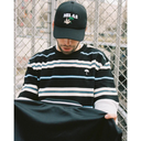 Person wearing a black and white striped sweater and cap with 'HELAS' branding, holding a black bag.
