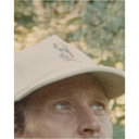Close-up of a person wearing a beige cap with a logo, outdoors.