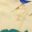 Close-up of a yellow shirt with a collar and buttons, featuring the brand 'Hélas'.