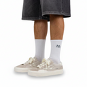White socks with a logo worn with beige sneakers on a white background