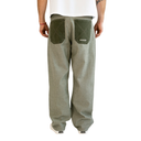 A person shown from the back wearing loose-fit olive green pants with contrasting darker green patch pockets and white sneakers, against a plain white background.
