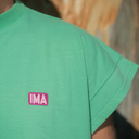 Green t-shirt with a pink 'IMA' logo on a blurred background