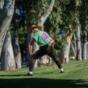 Person in a green shirt and brown pants playing golf in a park.