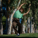Man in a green shirt and brown hat standing on a grassy area with trees in the background