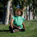 Man sitting on grass wearing a green shirt and straw hat with trees in the background