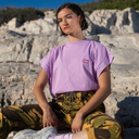 Person wearing a purple t-shirt with a logo and camouflage pants sitting on rocks.