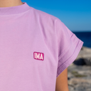 Person wearing a purple t-shirt with 'IMA' logo against a blurred natural background